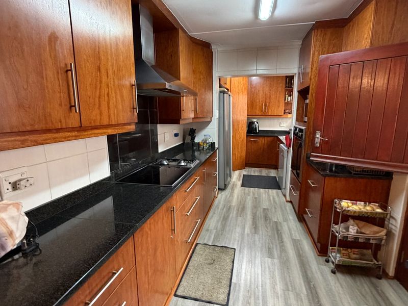 A functional kitchen featuring warm-toned wooden cabinetry, contrasting black granite countertops, modern laminate flooring, and integrated cooking appliances.