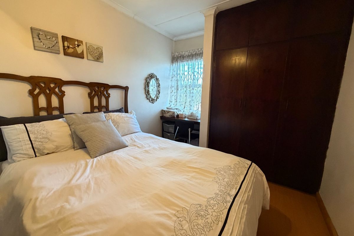 A bedroom featuring built-in wooden cupboards and a window with a security gate, providing functional storage and natural light.