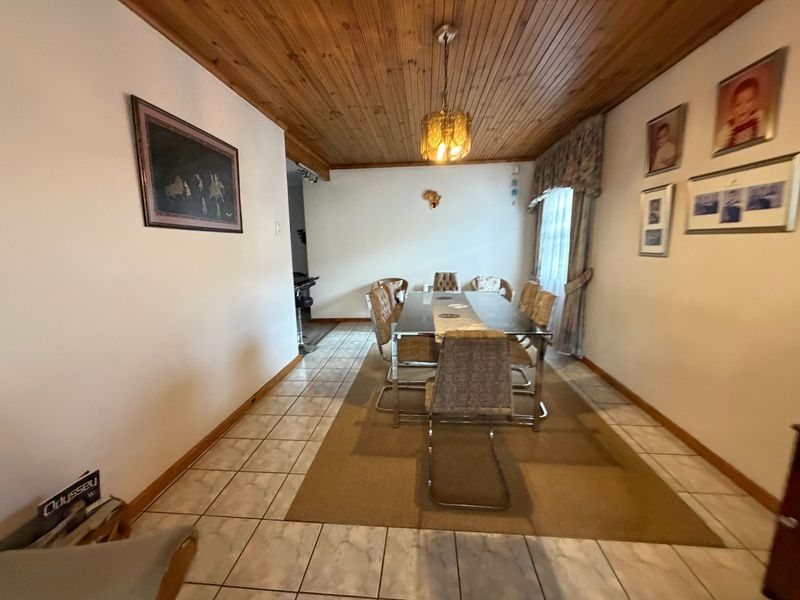 A dining room featuring ceramic floor tiles and a traditional timber tongue and groove ceiling with a central pendant light fixture.