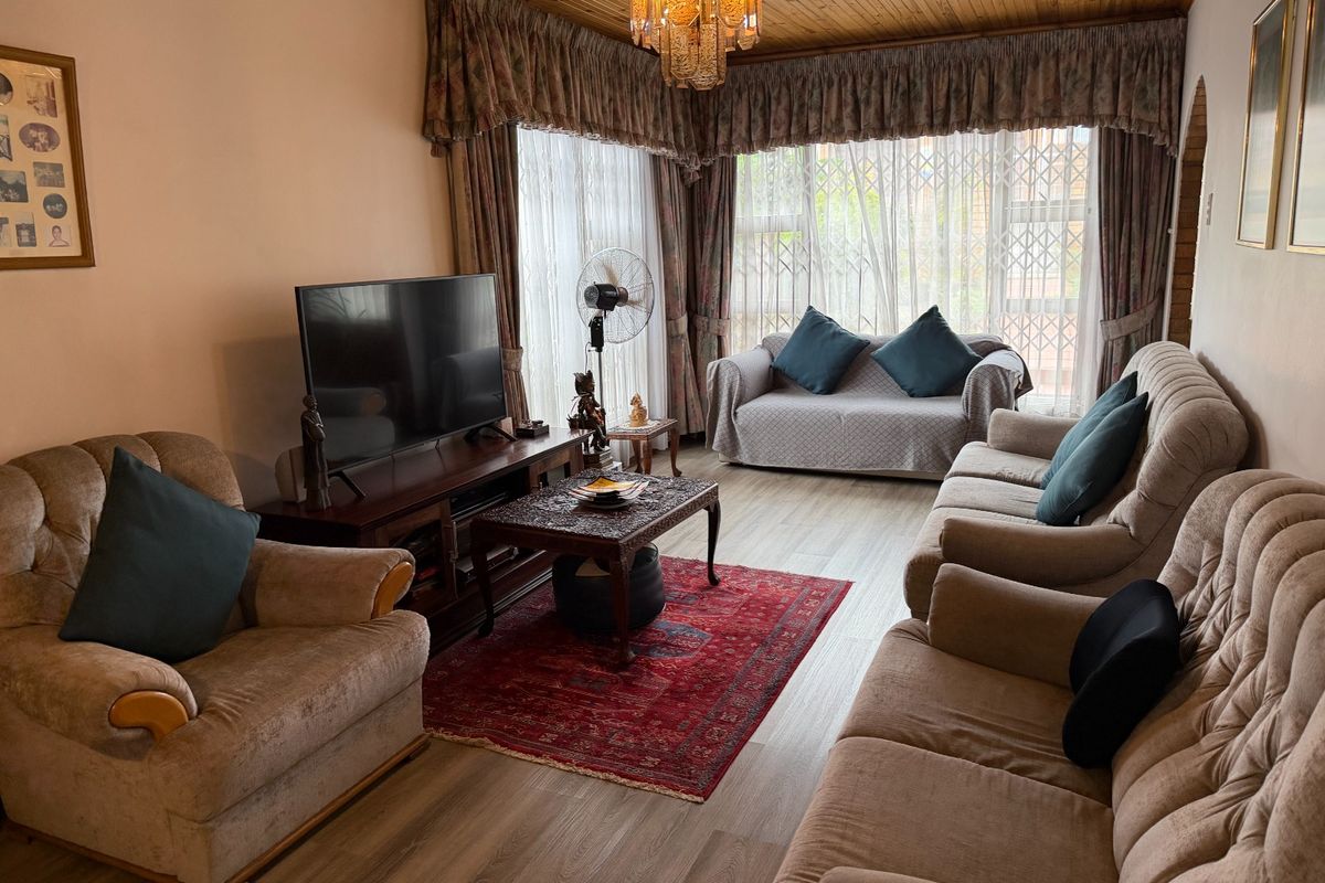 A comfortable living room featuring laminate flooring, a timber-paneled ceiling, and large windows with security gates.