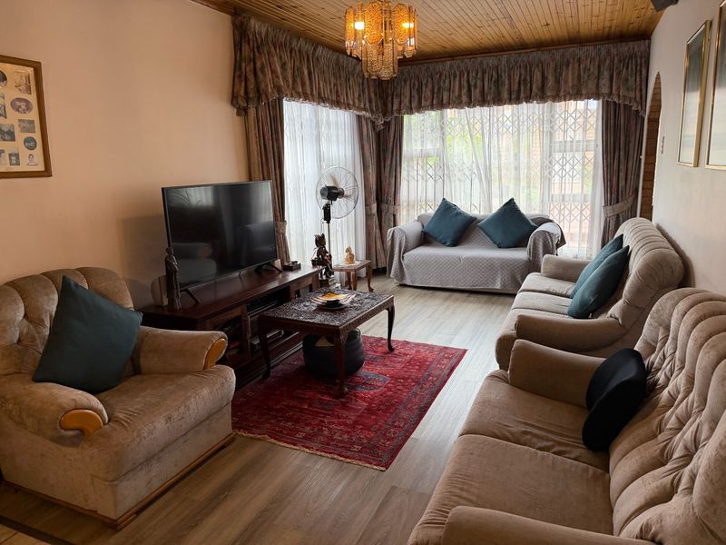 A comfortable living room featuring laminate flooring, a timber-paneled ceiling, and large windows with security gates.