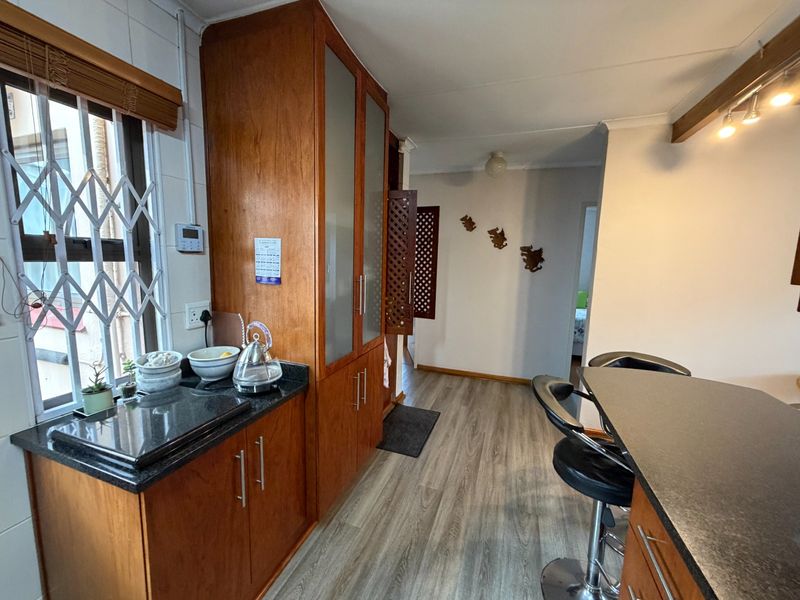 A functional kitchen featuring wood-finish cabinetry, dark granite countertops, a breakfast bar, and modern laminate flooring with a view toward the hallway.