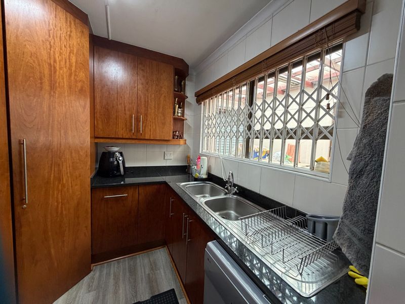 A functional kitchen featuring warm-toned wooden cabinetry, granite countertops, and a double stainless steel sink with a window security gate.