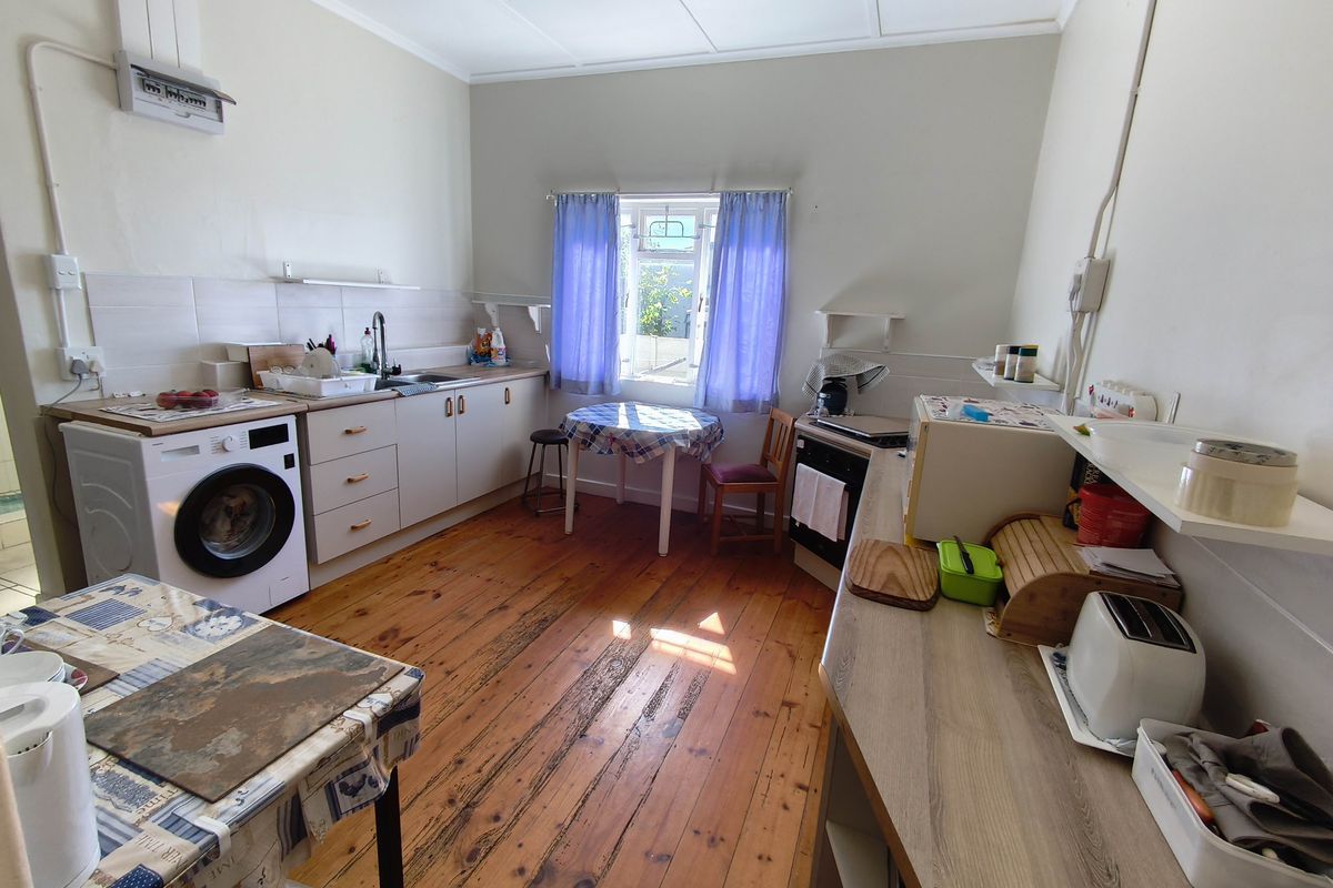 A functional kitchen featuring timber flooring, laminate countertops, tiled splashbacks, and built-in cabinetry with an integrated laundry space.