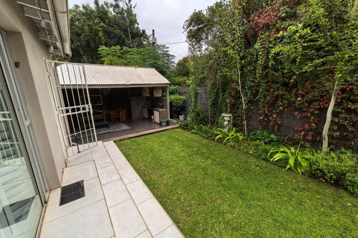 A well-maintained rear garden featuring a manicured lawn, a covered patio area with tiled flooring, and established climbing greenery along the boundary wall.