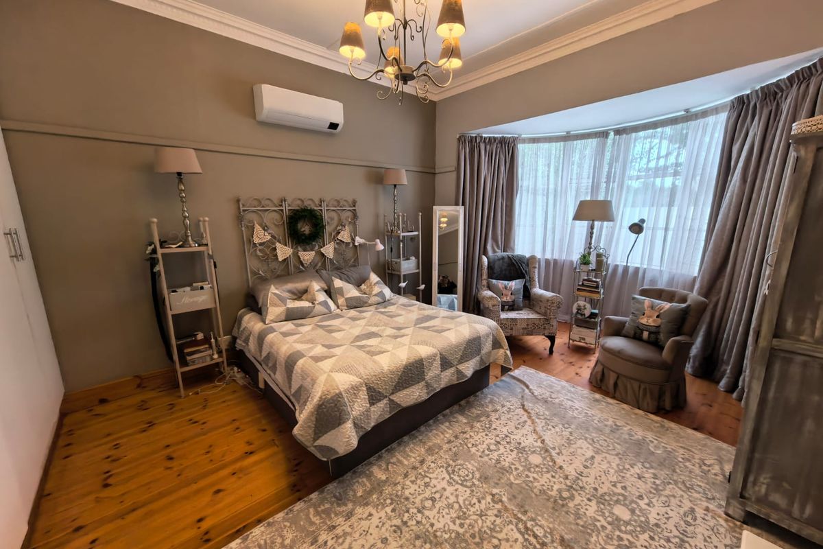 Spacious bedroom featuring polished timber flooring, a bay window with curtains, and a wall-mounted split-system air conditioner.