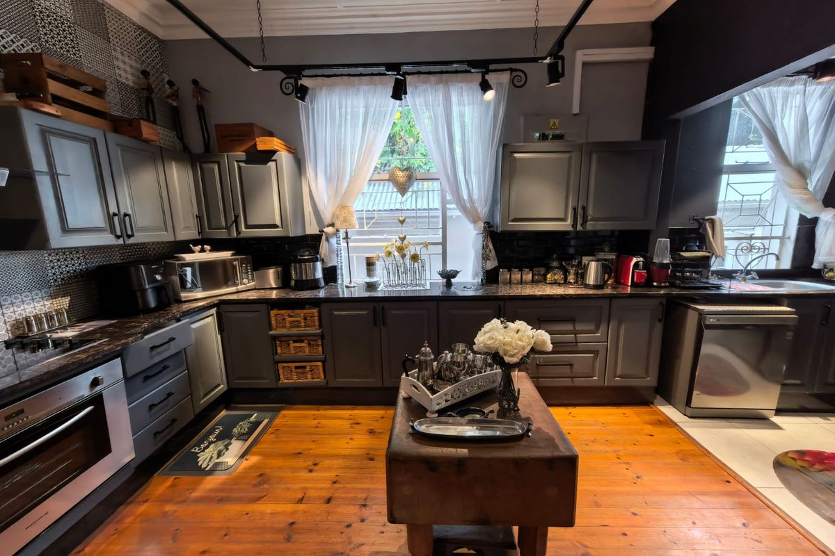 A well-appointed kitchen featuring dark grey cabinetry, stone countertops, integrated appliances, hardwood flooring, and stylish track lighting.
