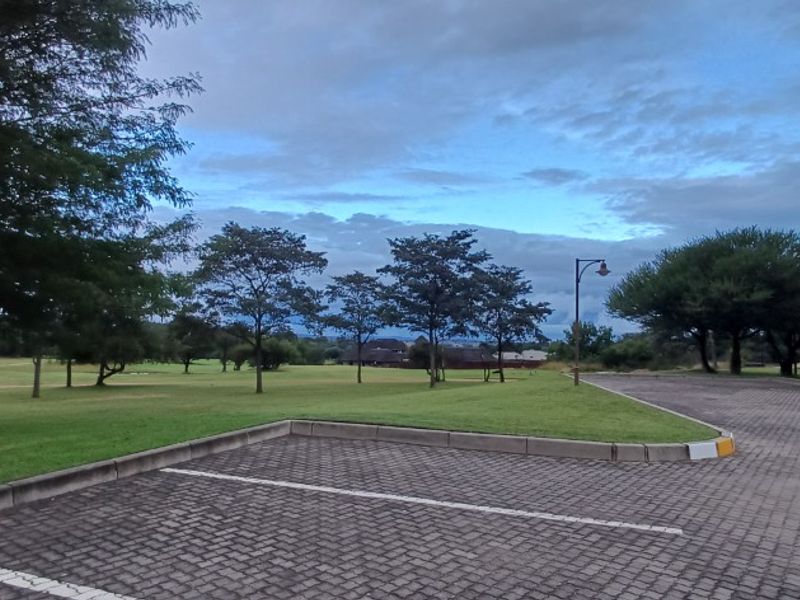 A well-maintained paved parking area adjacent to a spacious, manicured lawn and mature trees, providing a clean and accessible entrance to the property.