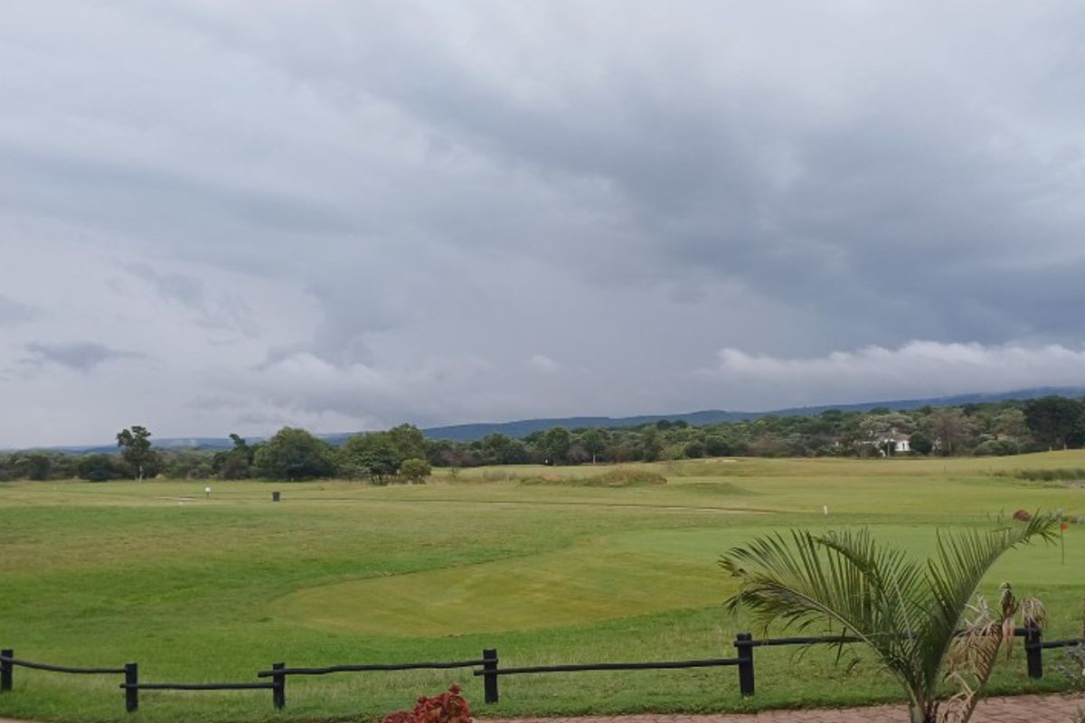 A scenic view overlooking a well-maintained golf course landscape with distant hills under a cloudy sky.