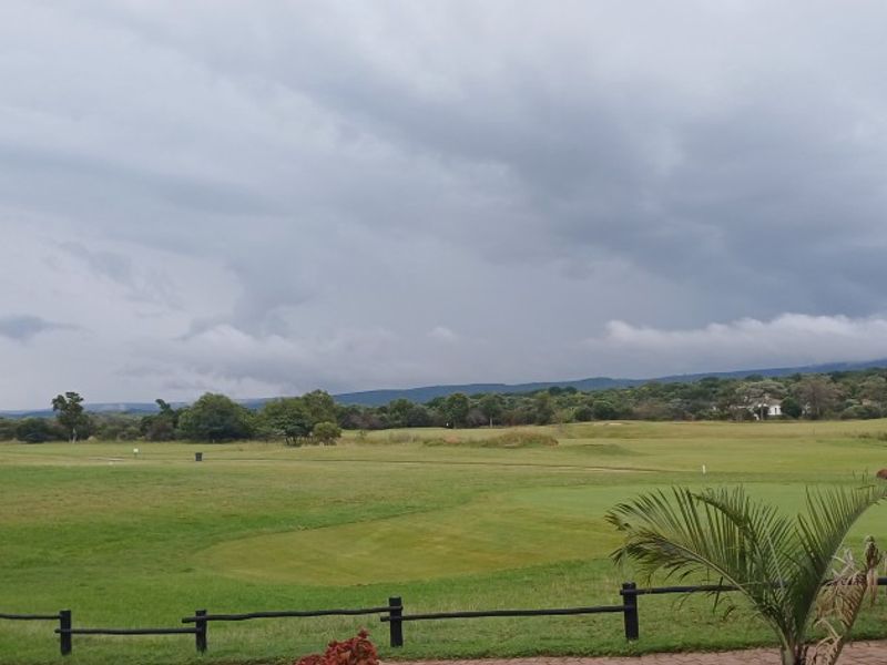 A scenic view overlooking a well-maintained golf course landscape with distant hills under a cloudy sky.