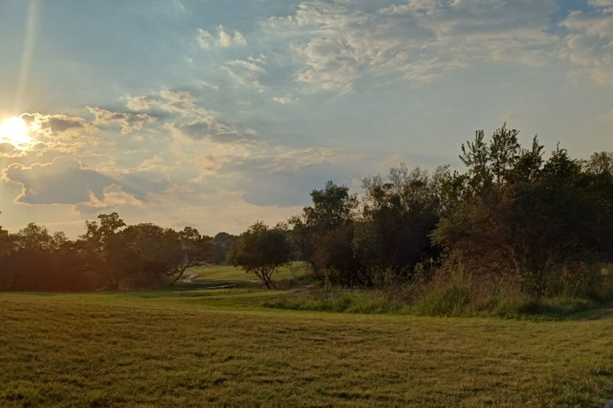 A scenic view of the vacant residential land featuring mature trees, open grassy areas, and a paved walkway under a sunset sky.