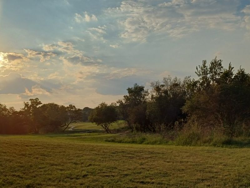 A scenic view of the vacant residential land featuring mature trees, open grassy areas, and a paved walkway under a sunset sky.