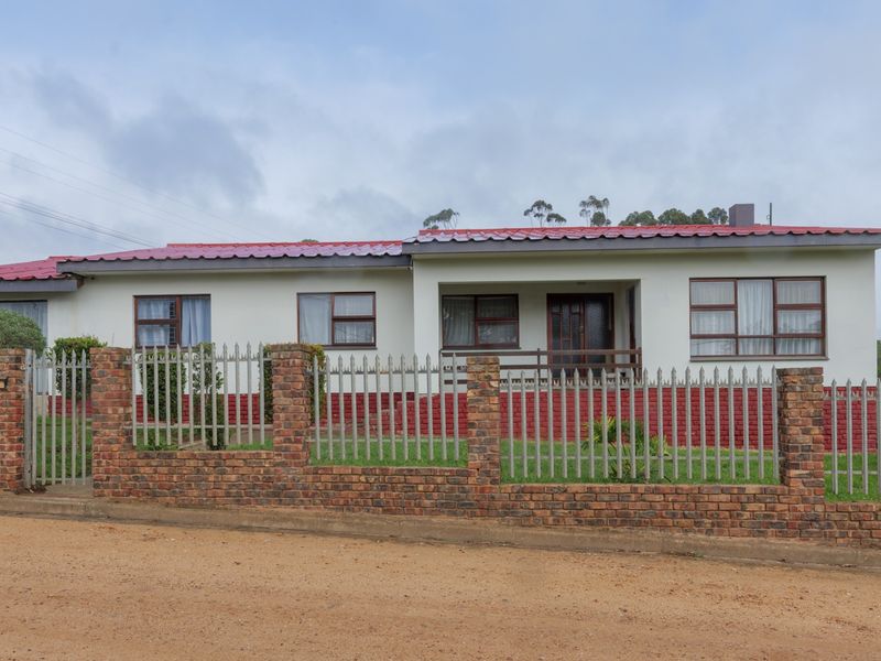 A single-story residential house featuring a red metal roof, white painted walls with brick accents, and a secure metal palisade fence.