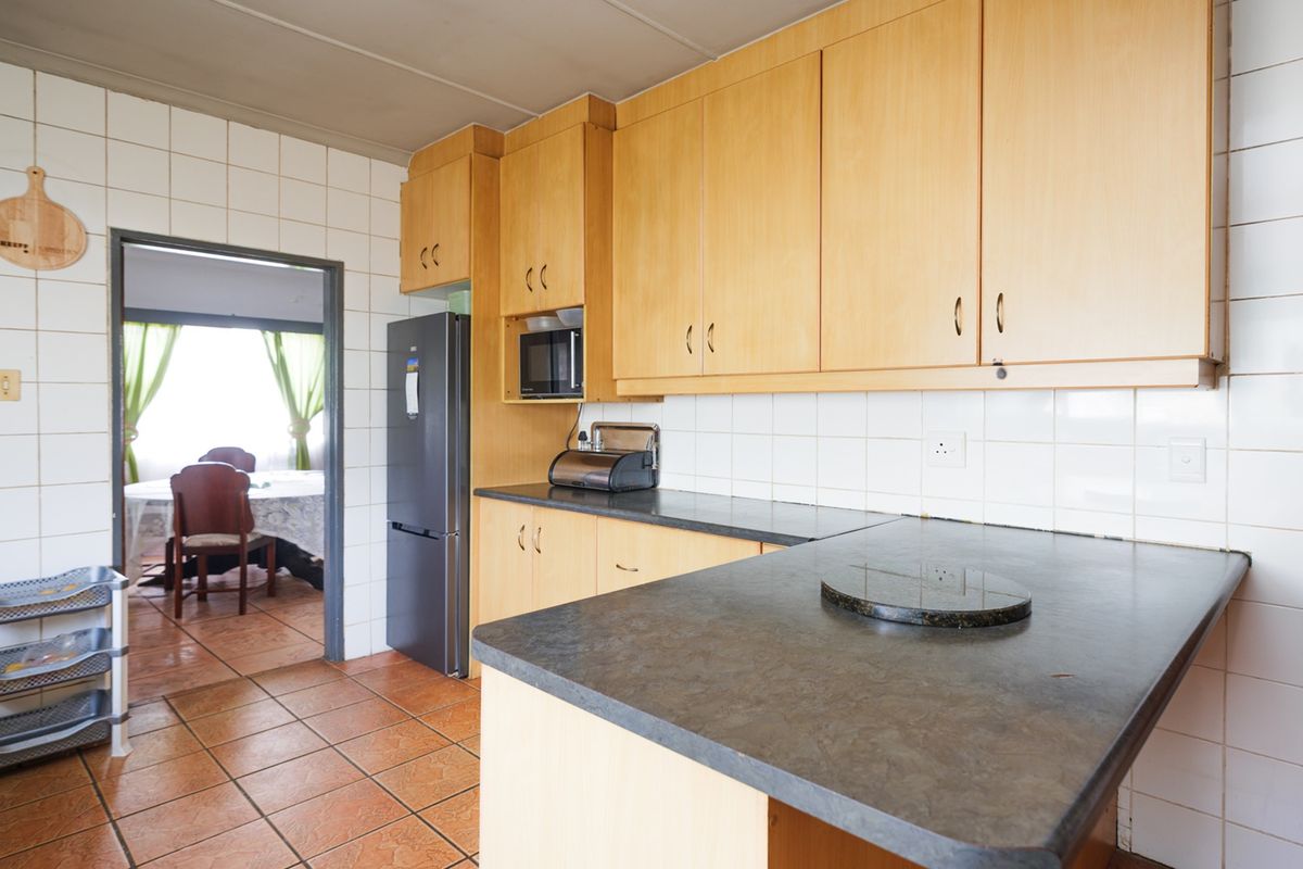 A functional kitchen featuring light wood-tone cabinetry, dark laminate countertops, and tiled wall finishes, providing a practical layout with direct access to the dining area.