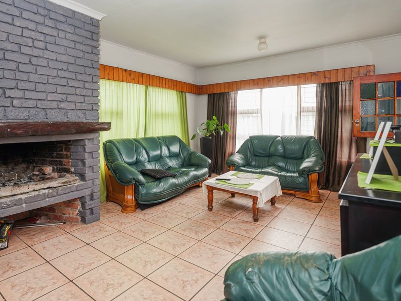 A living room featuring a prominent grey brick fireplace, tiled flooring, and a timber window pelmet, offering a traditional layout.