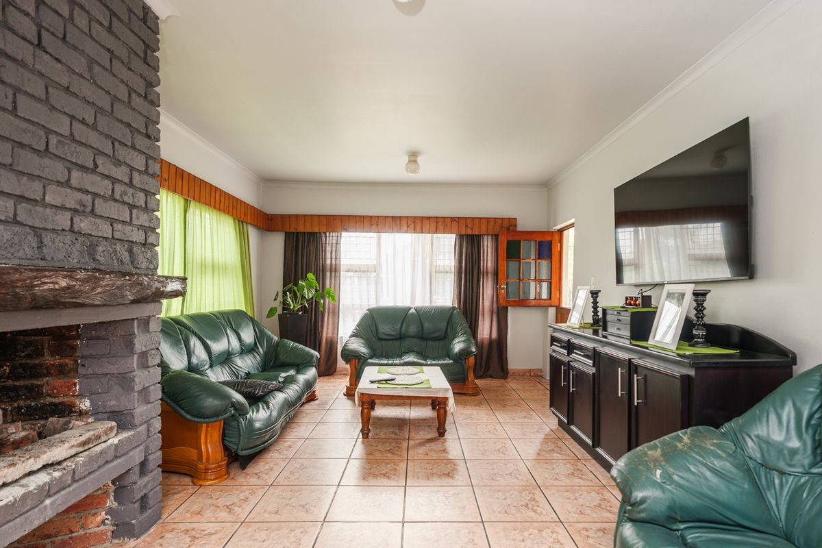 Spacious living room featuring a prominent brick fireplace, ceramic tile flooring, and large windows with timber pelmets.