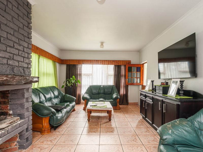 Spacious living room featuring a prominent brick fireplace, ceramic tile flooring, and large windows with timber pelmets.