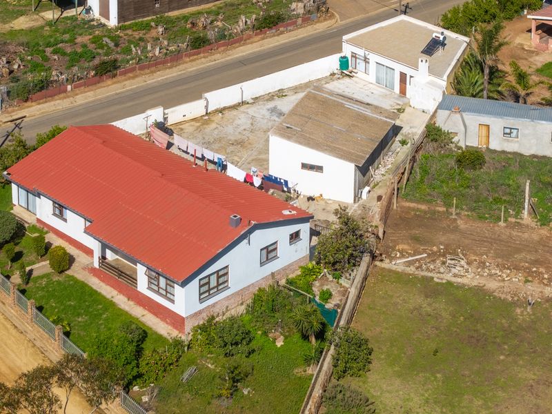 Aerial view of the property showing the main house with a red metal roof, adjacent outbuildings, and surrounding yard space.