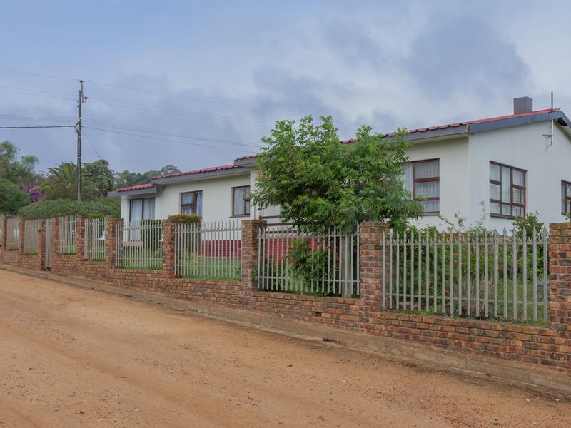 A single-story residential property featuring a brick boundary wall with metal palisade fencing, situated along an unpaved road.