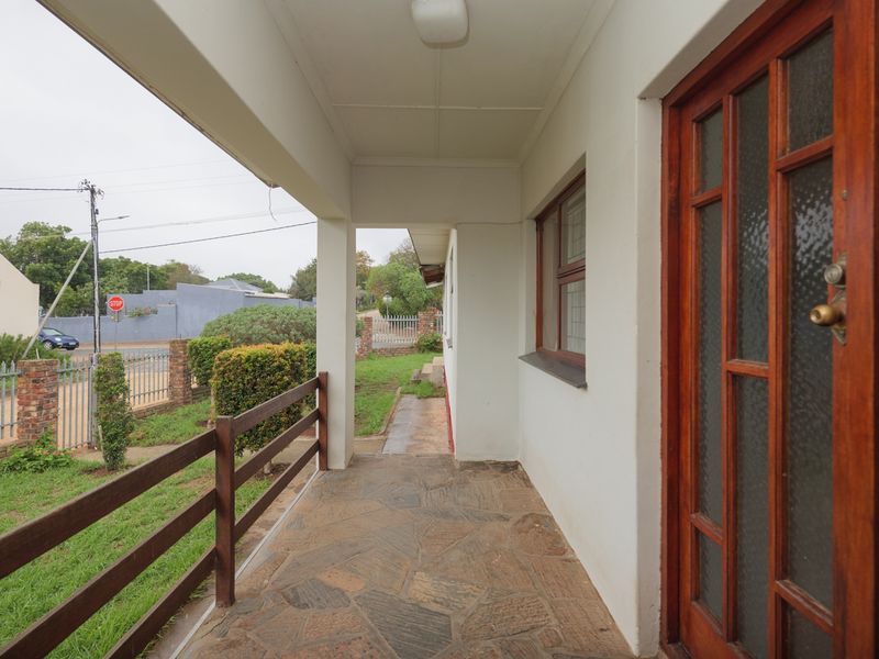 A covered patio area featuring stone paving, a timber railing, and a classic timber-framed glass entrance door.