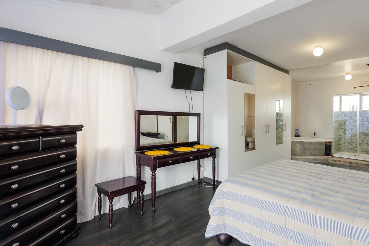Spacious bedroom featuring built-in cupboards, laminate flooring, and an open-plan en-suite bathroom with a bathtub and shower.