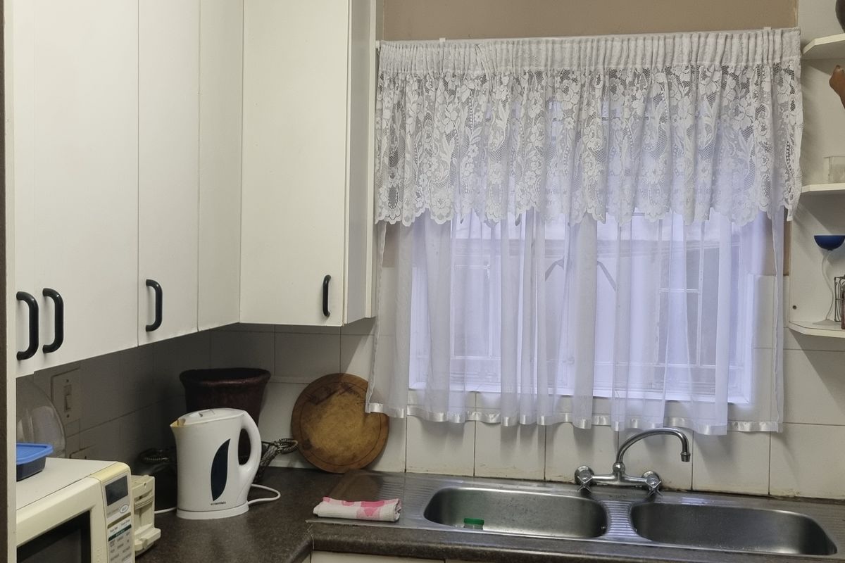 A functional kitchen area featuring white cabinetry, a double bowl stainless steel sink, tiled splashback, and built-in corner shelving.