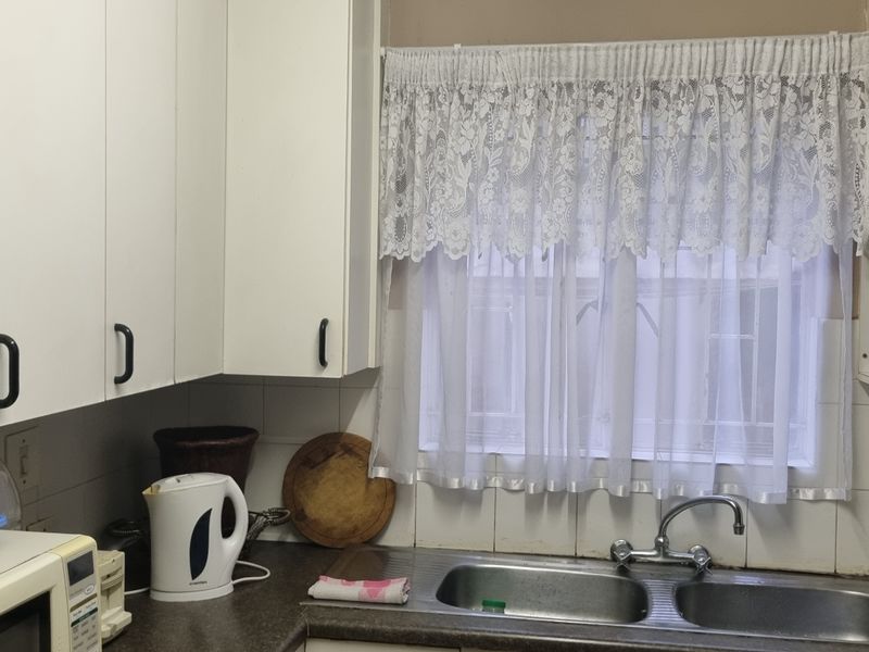 A functional kitchen area featuring white cabinetry, a double bowl stainless steel sink, tiled splashback, and built-in corner shelving.