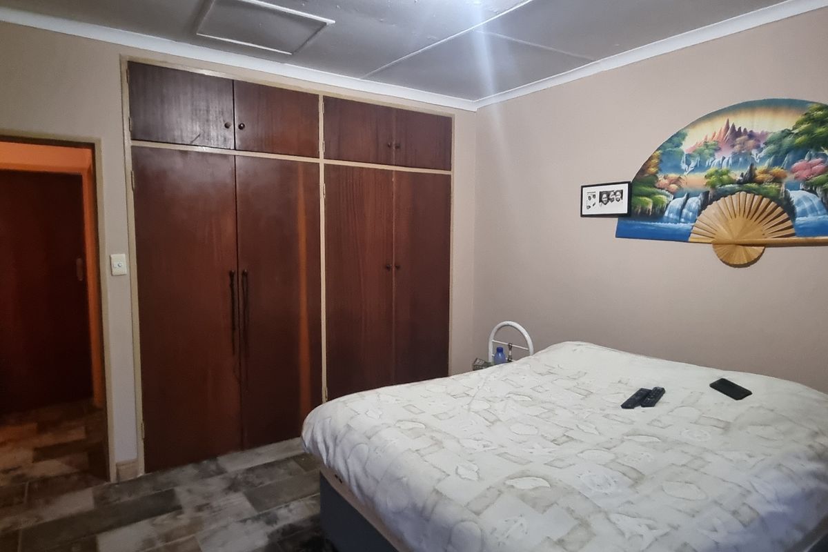 A bedroom featuring built-in wooden cupboards, tiled flooring, and a ceiling access hatch, offering a functional space with dated finishes.