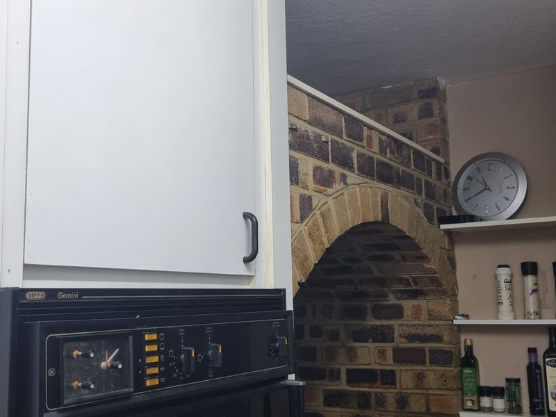 Kitchen area featuring a distinctive brick arch architectural element, built-in oven, and fixed shelving, showcasing a dated aesthetic with potential for modernization.