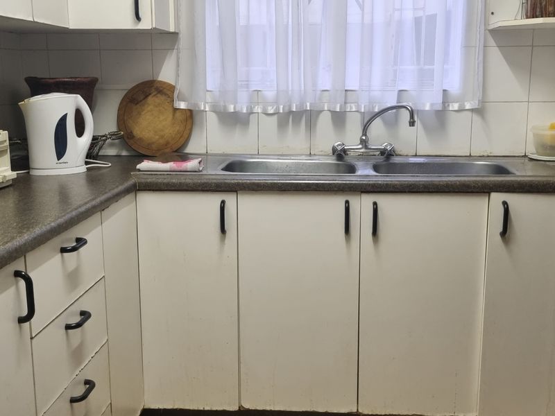 A compact kitchen featuring laminate countertops, a double basin stainless steel sink, and white cabinetry with a tiled backsplash.