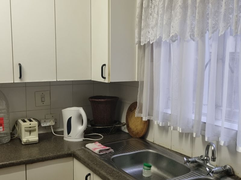 A functional kitchen area featuring white cabinetry, laminate countertops, a stainless steel sink, and tiled splashbacks, offering a practical layout for daily use.