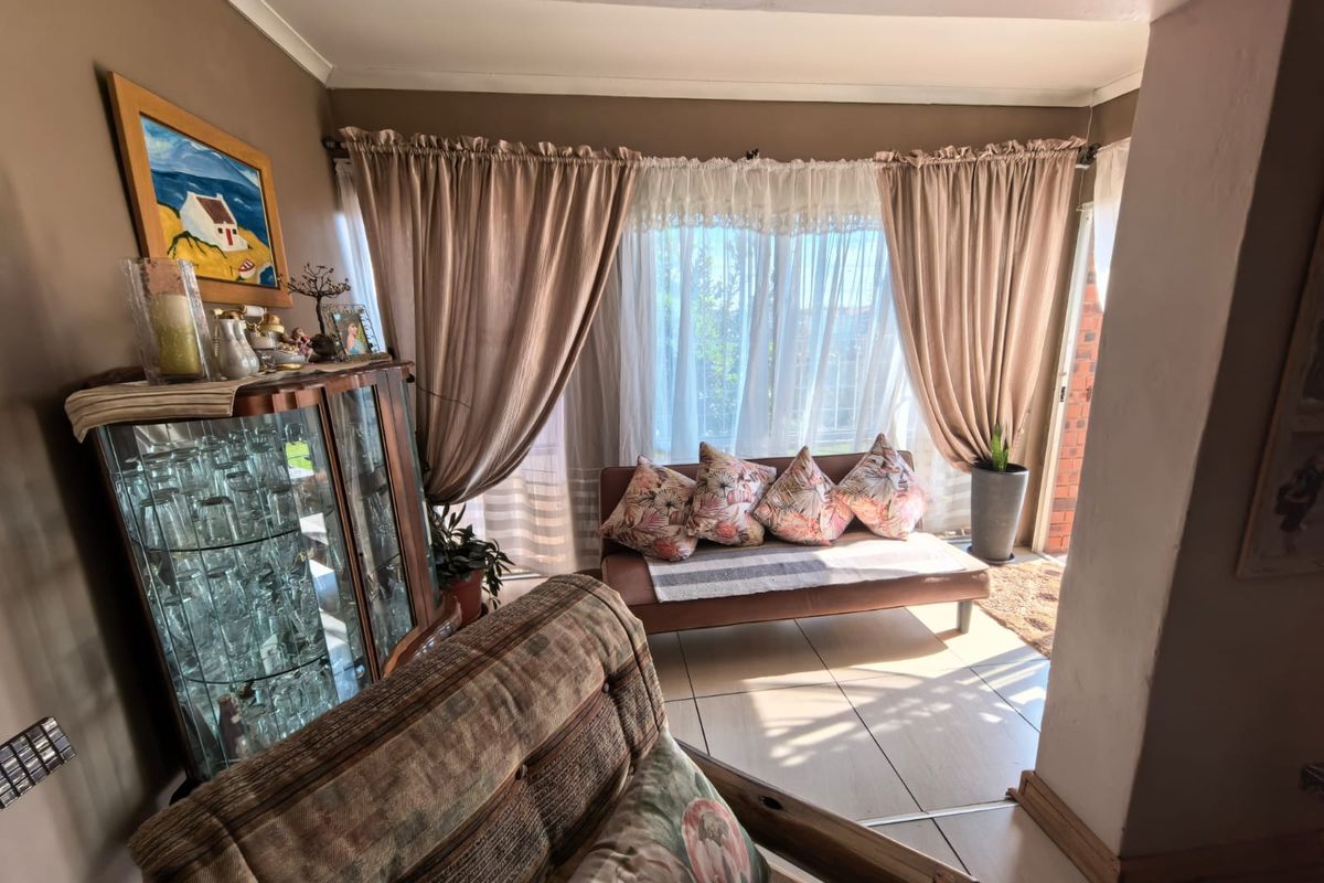 A sunlit living area featuring tiled flooring and large windows with curtains, providing a comfortable and bright space for relaxation.