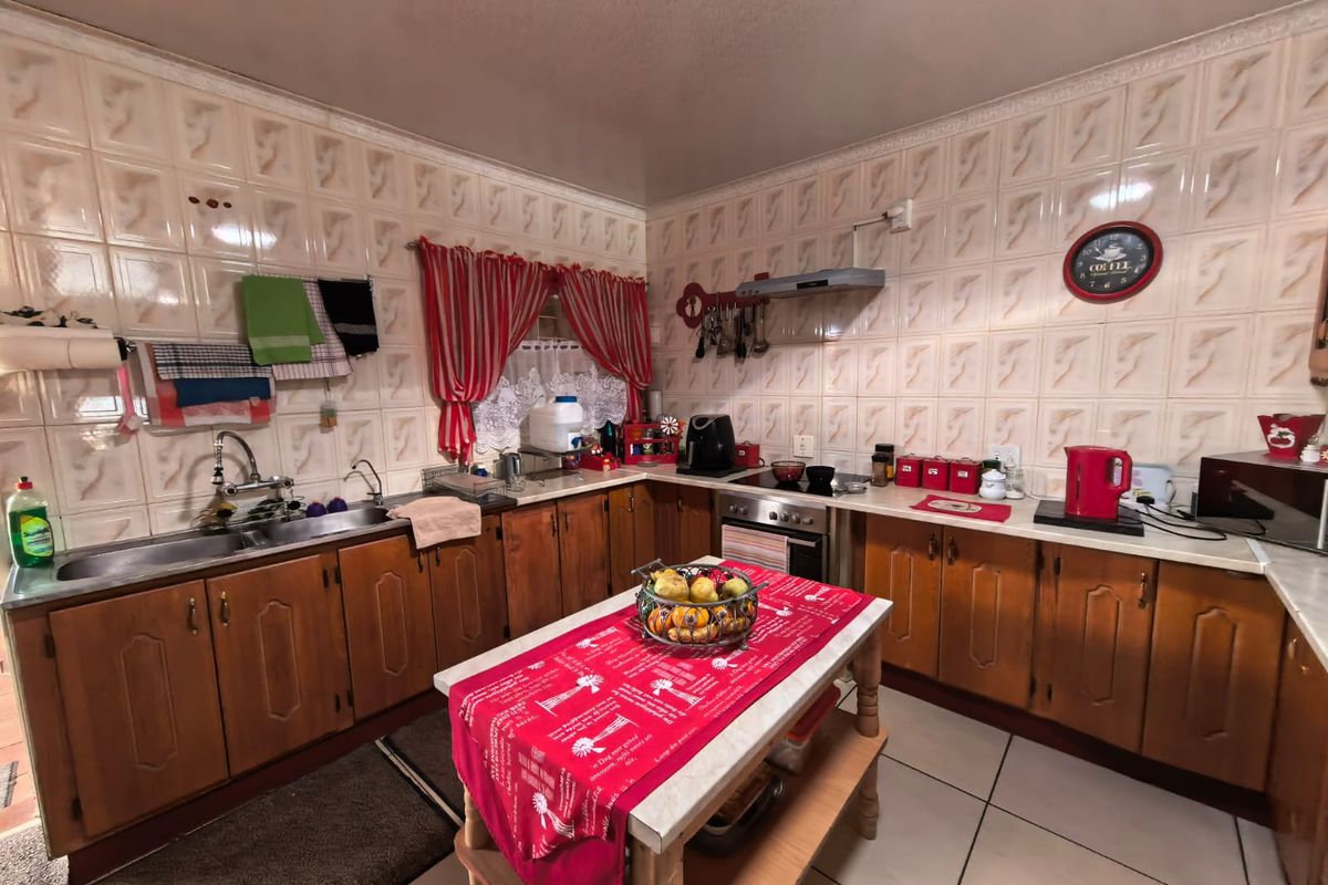 A functional kitchen featuring wooden cabinetry, tiled splashbacks, a double sink, and an integrated stove with an extractor fan.