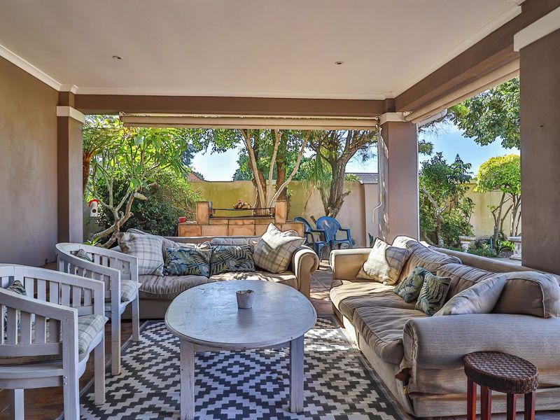 A covered patio area featuring a built-in outdoor braai, tiled flooring, and structural pillars, overlooking the garden and pool area.
