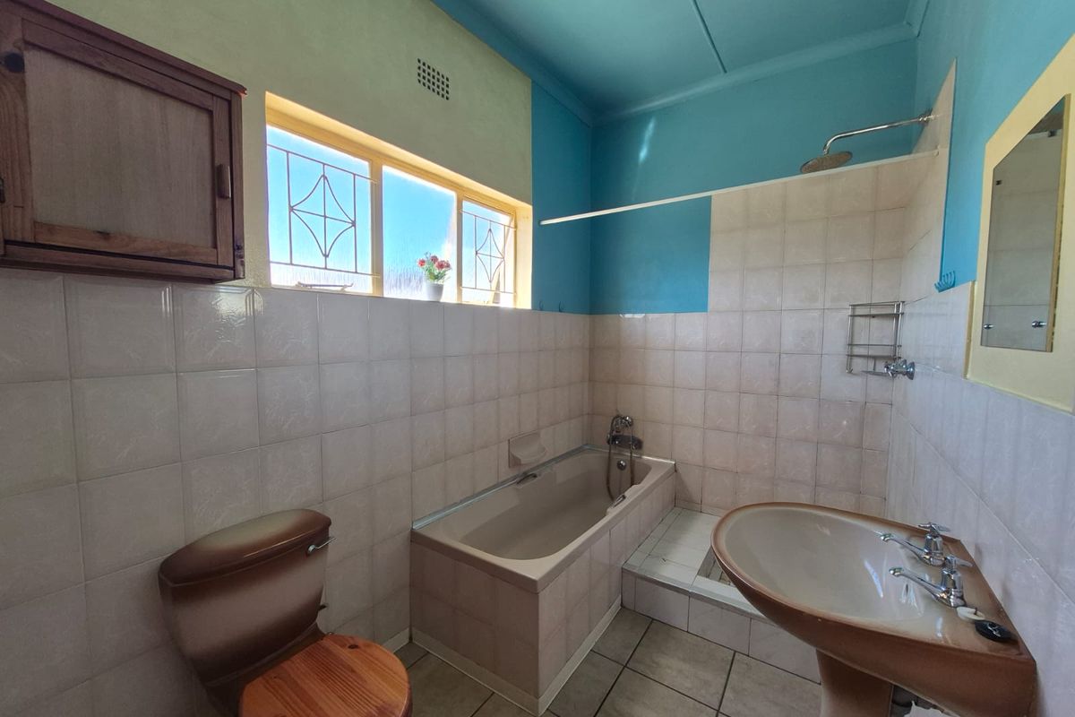 A dated bathroom featuring a built-in bathtub, pedestal basin, and toilet, with tiled walls and a high-contrast painted ceiling.