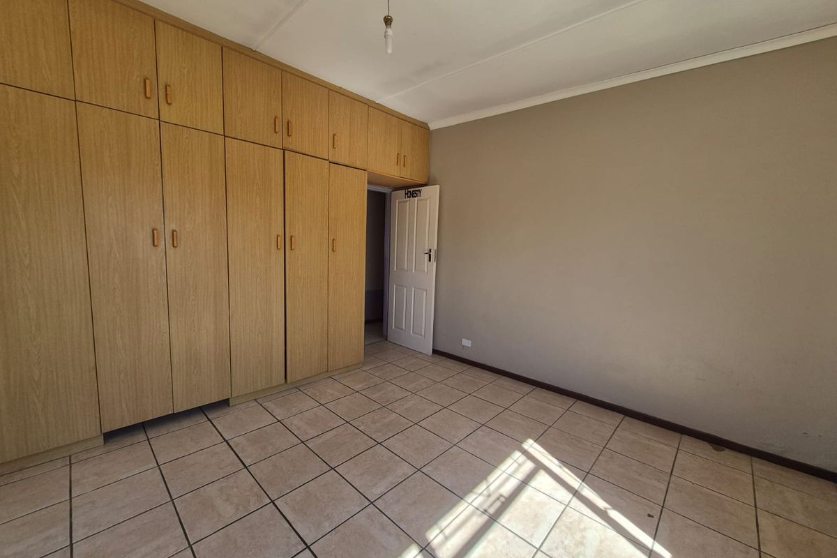 A bedroom featuring built-in wooden cabinetry, tiled flooring, and a standard interior door, offering a functional and neutral living space.