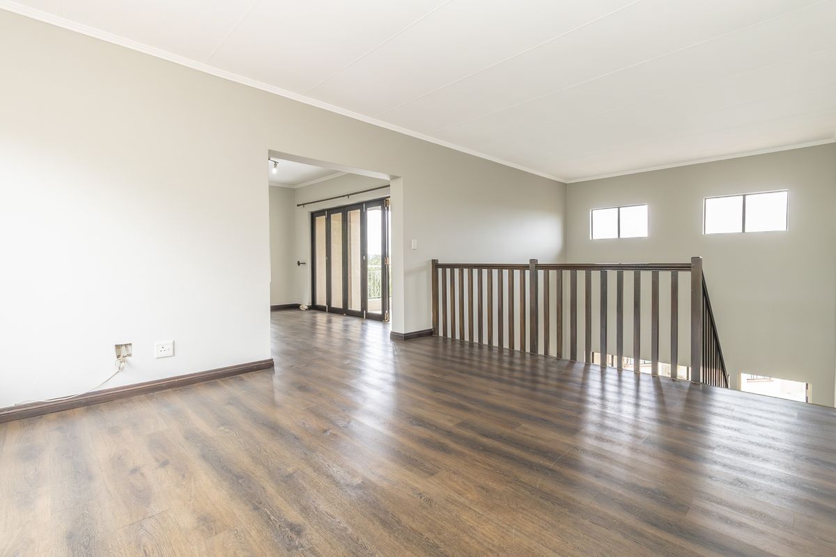 Spacious landing or living area featuring dark laminate flooring, a timber balustrade overlooking the staircase, and access to an adjoining room via sliding doors.