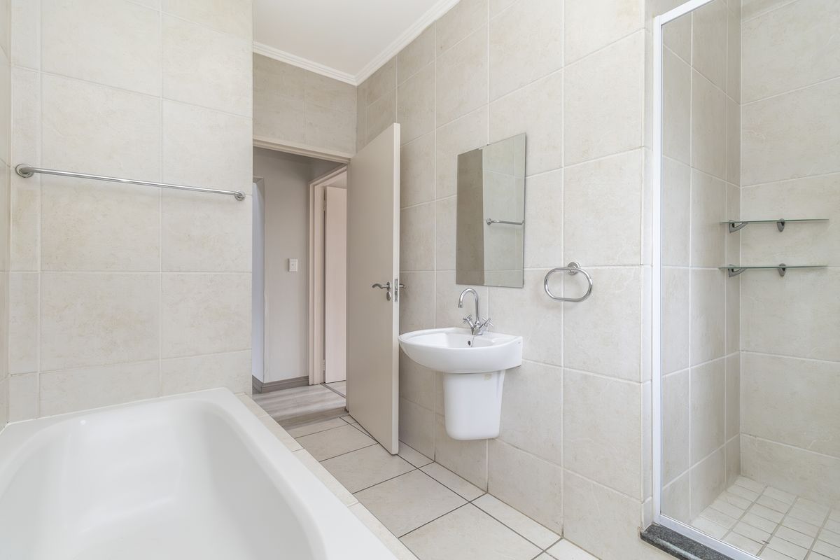 A clean, neutral-toned bathroom featuring a pedestal basin, a bathtub, and a separate shower enclosure with tiled finishes throughout.