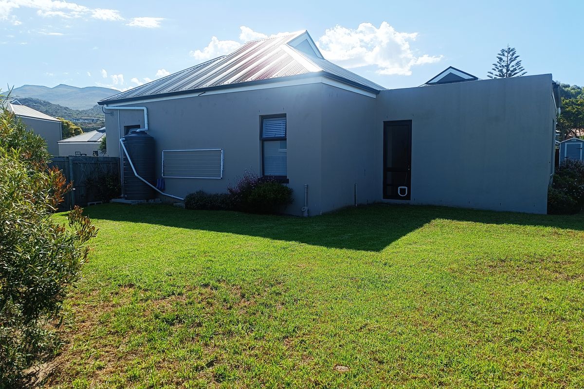 Rear view of the property featuring a well-maintained lawn, metal roof, and an installed rainwater harvesting tank.