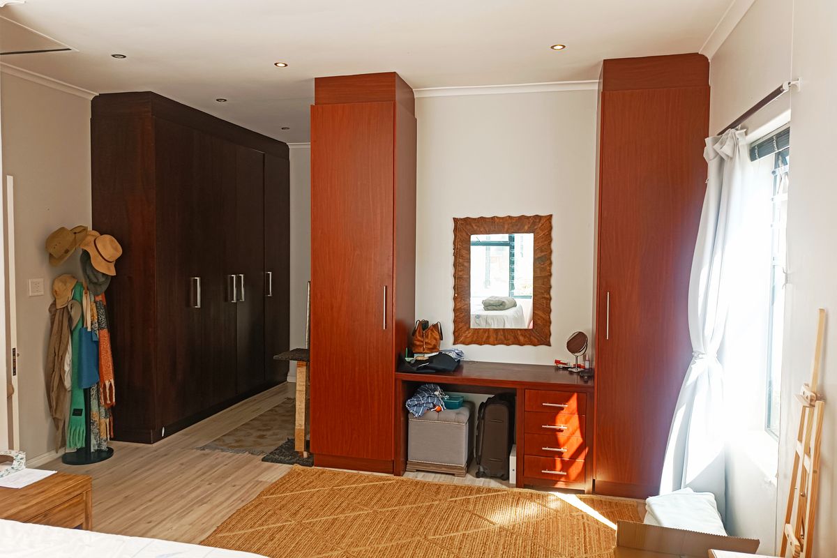 Spacious bedroom featuring extensive dark wood built-in cabinetry, a matching integrated vanity unit, recessed lighting, and light-toned laminate flooring.