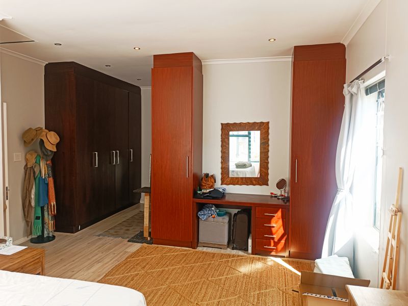 Spacious bedroom featuring extensive dark wood built-in cabinetry, a matching integrated vanity unit, recessed lighting, and light-toned laminate flooring.
