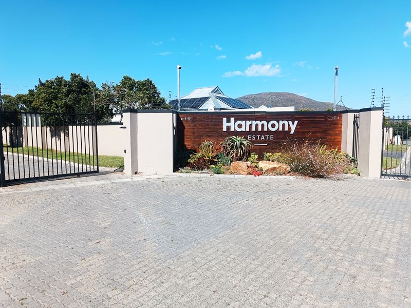 The entrance to Harmony Estate featuring a modern signage wall, paved driveway, and secure perimeter fencing.