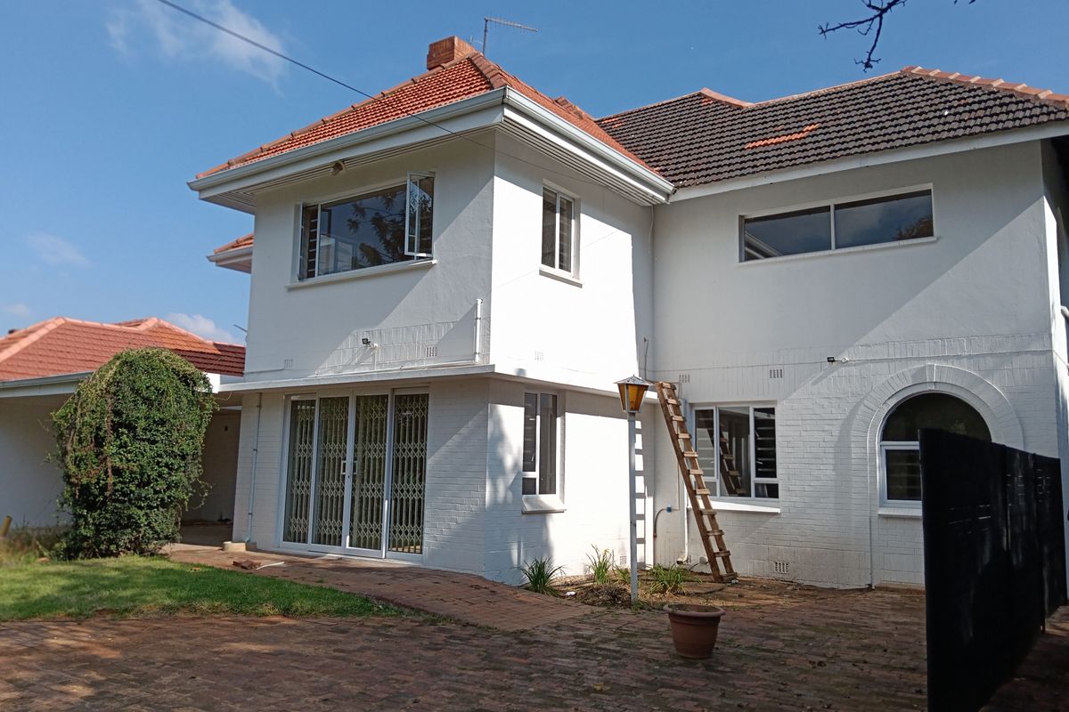 Rear view of a two-story residential property featuring white painted brick walls, tiled roofing, and paved courtyard area.