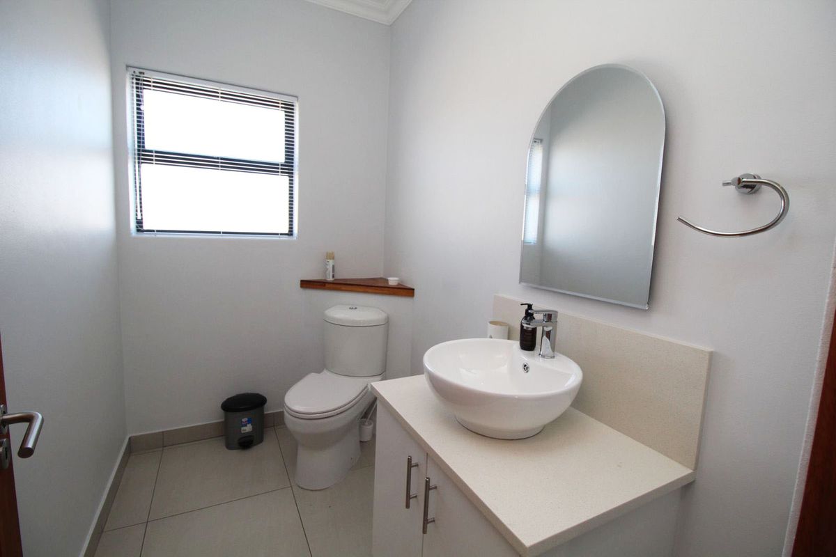 A clean and modern bathroom featuring a white vanity with a vessel sink, a wall-mounted mirror, and a toilet.