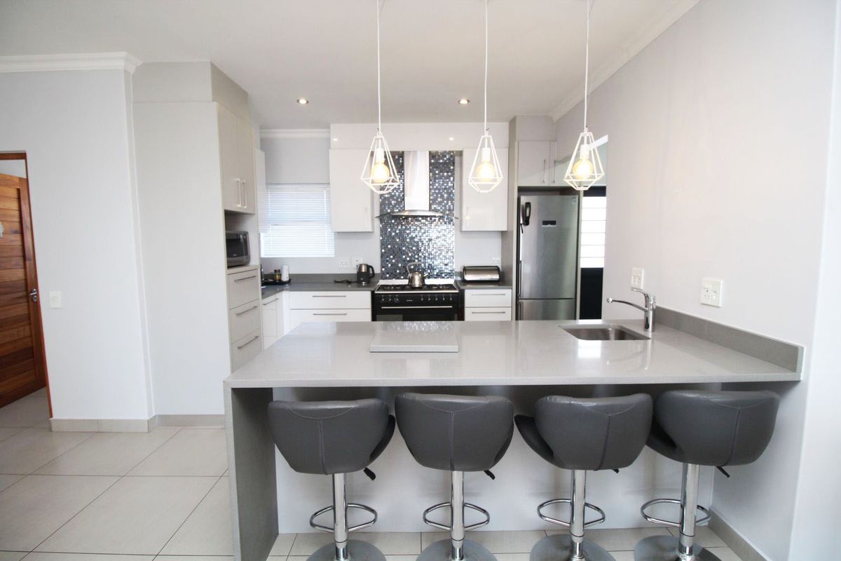 Modern kitchen featuring a central island with a built-in sink, stone countertops, mosaic tile backsplash, and stainless steel appliances.