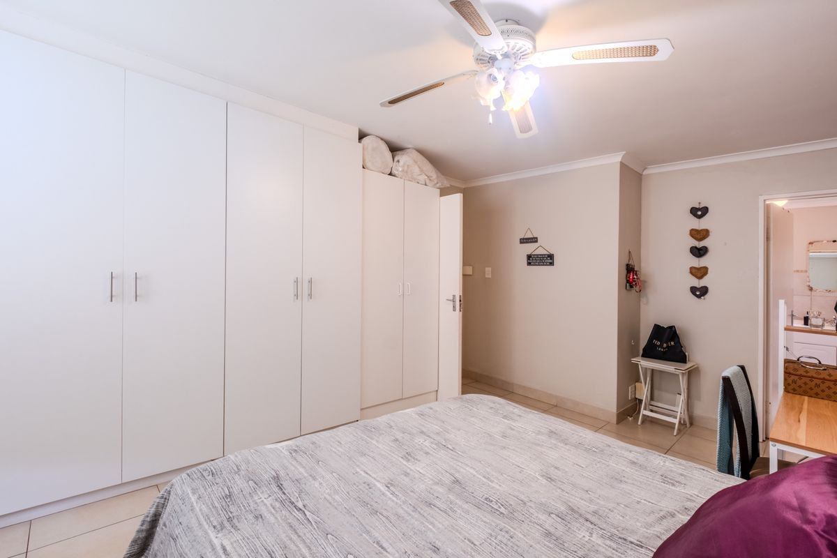 A well-maintained bedroom featuring extensive white built-in cupboards, a ceiling fan, and neutral tiled flooring.