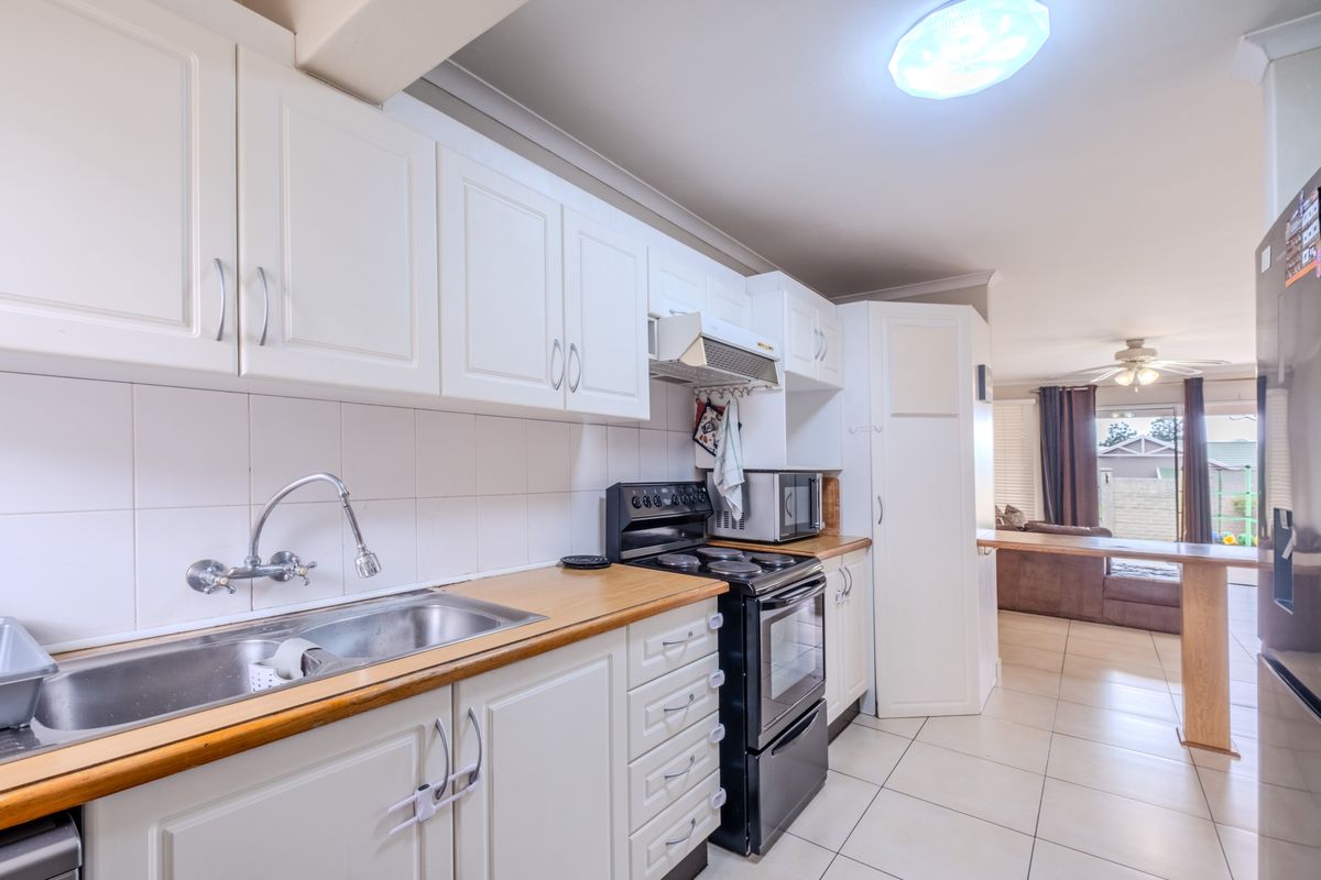 Functional kitchen featuring white cabinetry, wooden countertops, tiled splashbacks, and a breakfast bar, flowing into the adjacent living area.