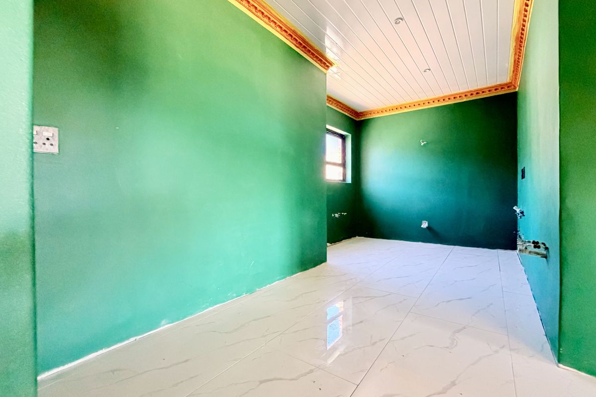 An empty, unfinished kitchen space featuring white marble-look floor tiles, green walls, and a white tongue and groove ceiling with decorative cornicing.