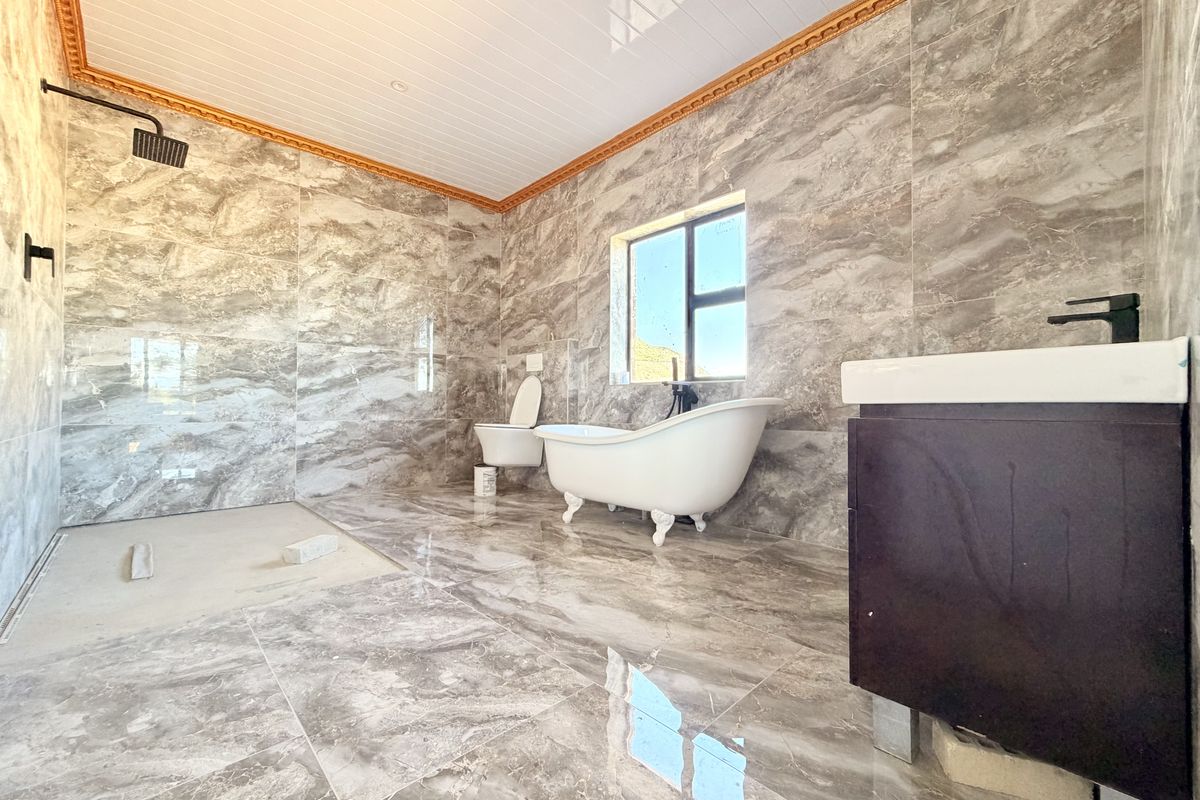 Spacious bathroom featuring marble-effect tiling, a freestanding bathtub, and a modern vanity. The shower area requires final finishing touches.