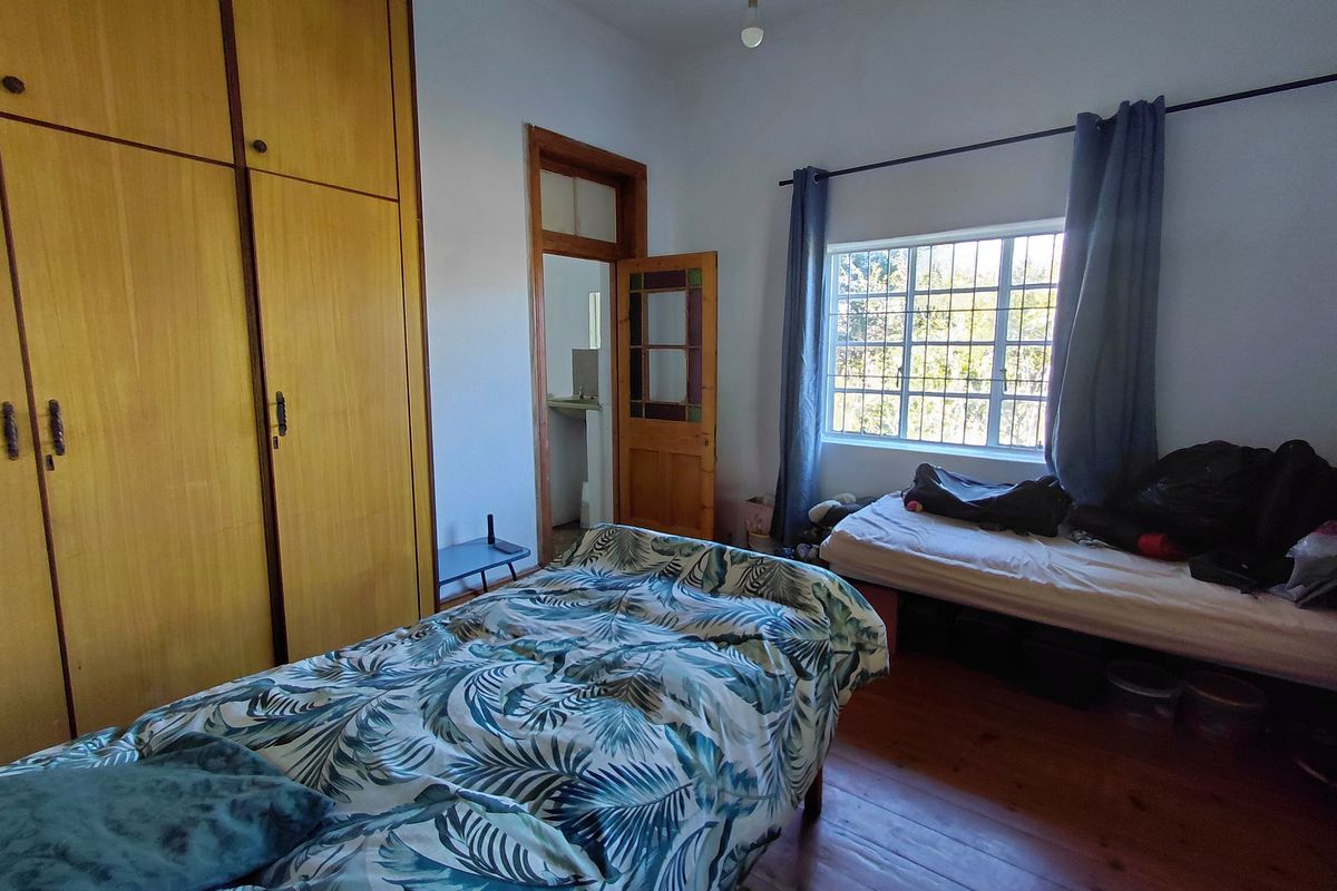 A bedroom featuring original timber flooring, a large built-in wooden wardrobe, and natural light through a window with security bars.